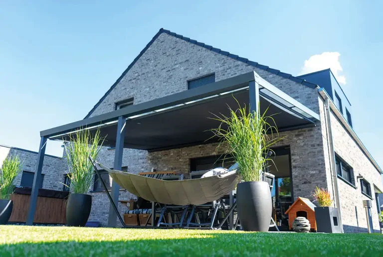 Anthrazitfarbene, wandmontierte Terrassenüberdachung aus Aluminium an modernem Einfamilienhaus mit Sitzgruppe im Garten