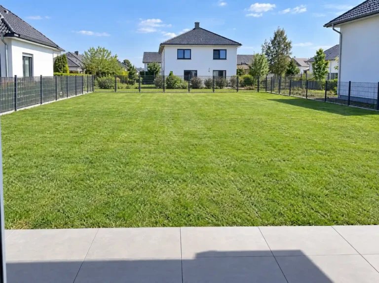 Eingezäunter Garten mit gepflegtem Rasen, im Hintergrund ein weißes Einfamilienhaus.
